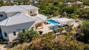 Et moderne hus med swimmingpool, omgivet af frodig vegetation og andre boliger.