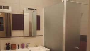 Een badkamer met een witte wasbak, donkere kastjes, een spiegel en een douchecabine met glas-in-lood.