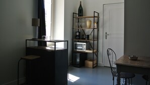 Een kleine keuken met een zwart aanrecht, een magnetron, een koffiezetapparaat en een wijnfles op een plank.