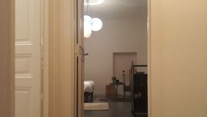 Een gang die leidt naar een slaapkamer met een bed, een bureau en een stoel.