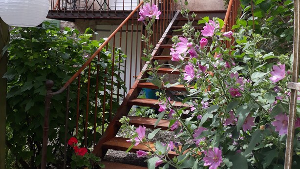Een houten trap met roze bloemen, een witte lantaarn en een balkon met een tafel en stoelen.