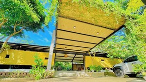 Un espace extérieur abrité, avec un bâtiment jaune, une allée pavée et un véhicule garé.