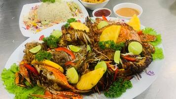 Una bandeja de mariscos con pescado a la parrilla, cangrejo y verduras, acompañada de arroz, papas fritas y salsas para mojar.
