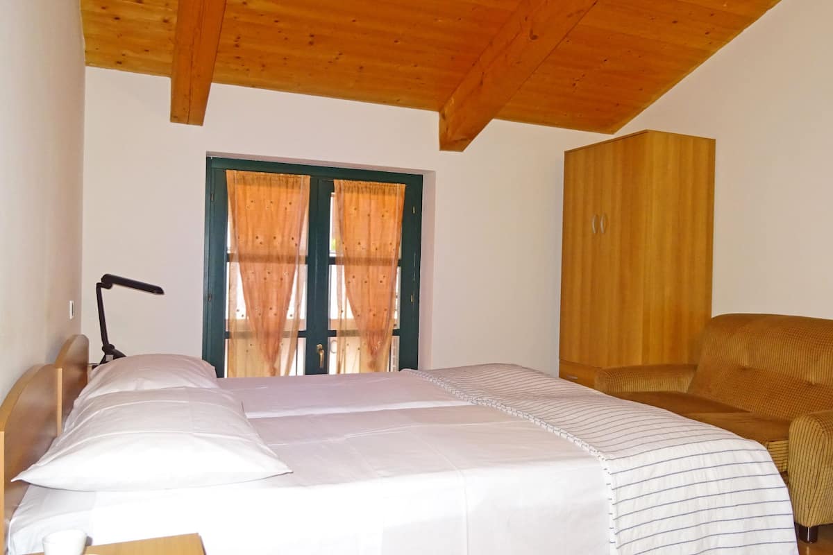 Ein Schlafzimmer mit Holzboden, einem Bett mit weißer Bettwäsche, einem Holzschrank und einem Fenster mit Vorhängen.