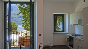 A kitchen with a view of a lake and mountains, a dining area with a chair, and a balcony with a gate. - Holideal Campione Bed & Surf (Tremosine)