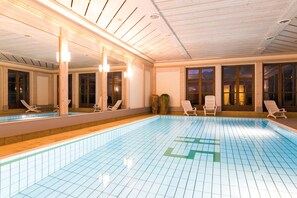 Piscina interna com revestimento de azulejos, paredes de madeira e várias janelas.