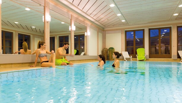 An indoor swimming pool with clear blue water, wooden ceiling, and large windows.