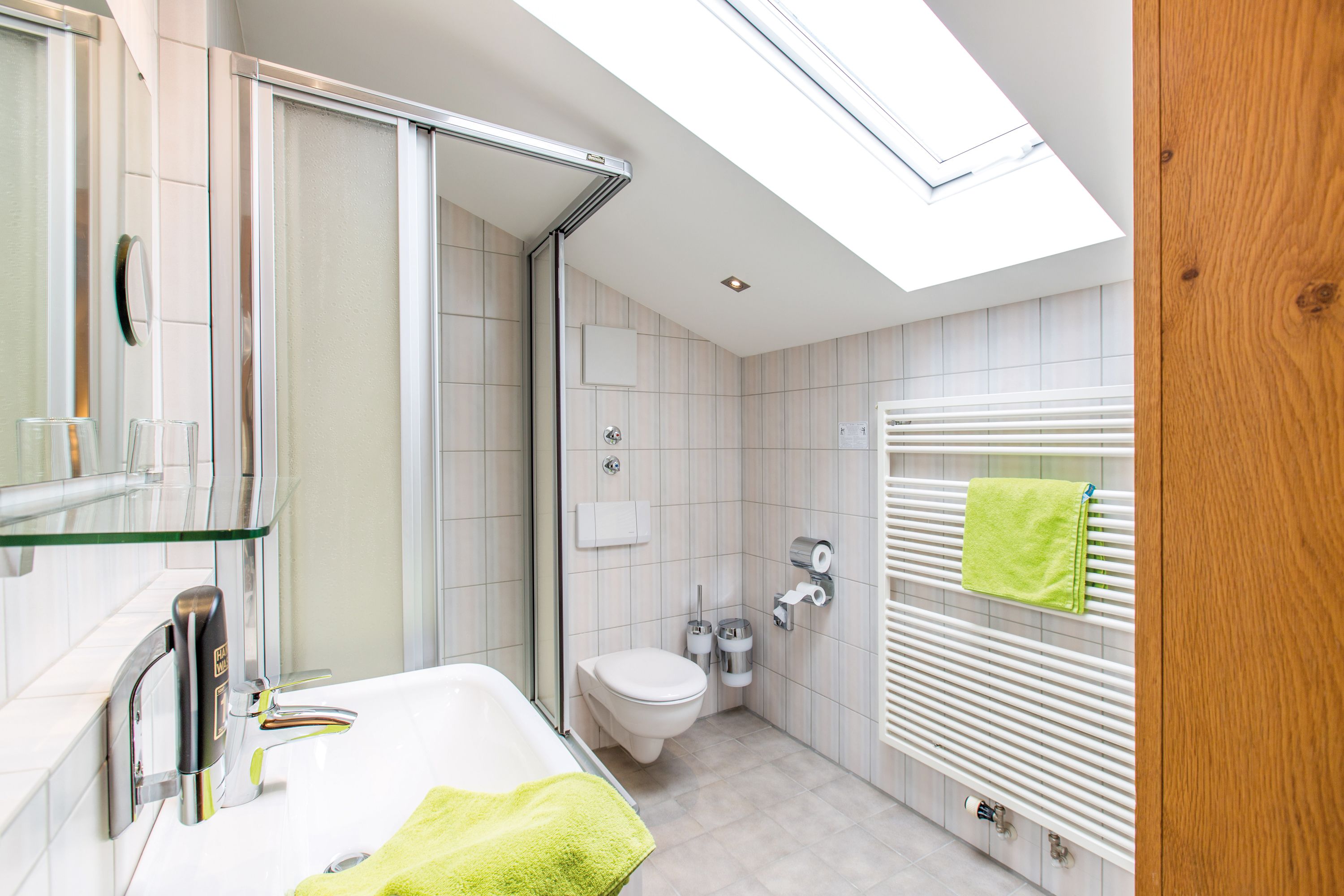 Ein modernes Badezimmer mit Duschkabine aus Glas, einer weißen Toilette, einem integrierten Waschbecken und einem Handtuchhalter mit einem grünen Handtuch.