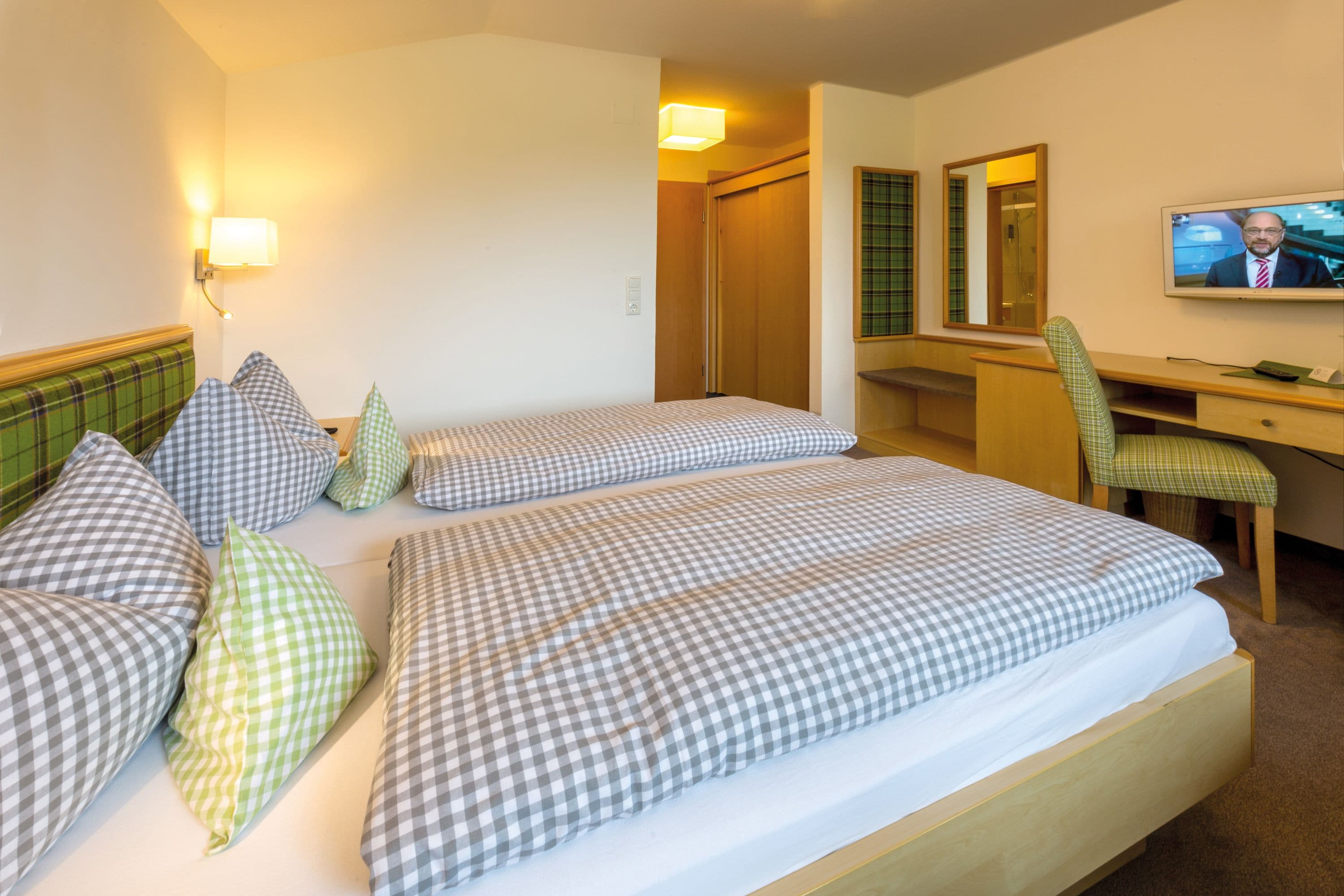 A hotel room with two beds, a desk, a chair, a television, and a mirror.