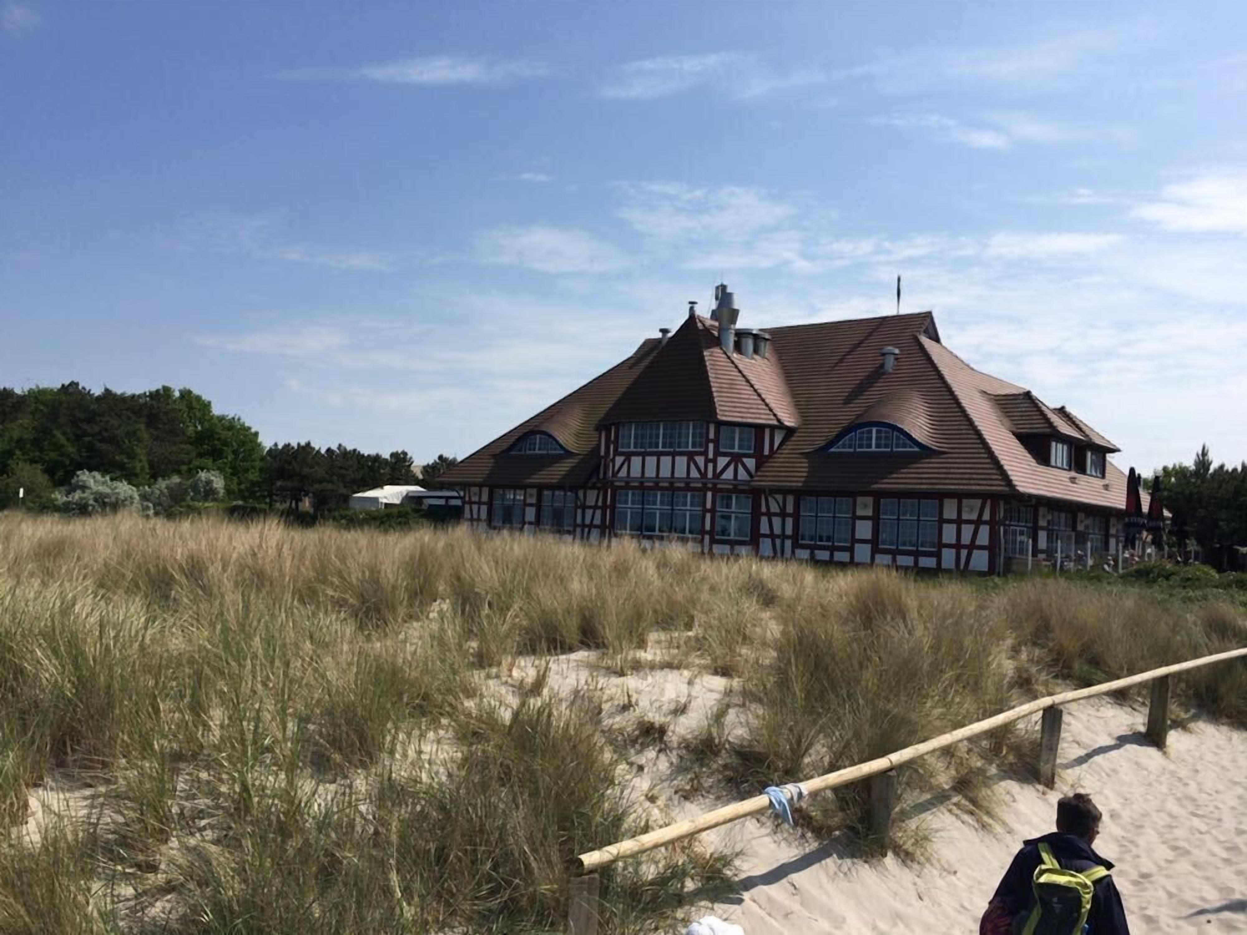A large, traditional building with a steep roof, surrounded by tall grass and sand dunes.