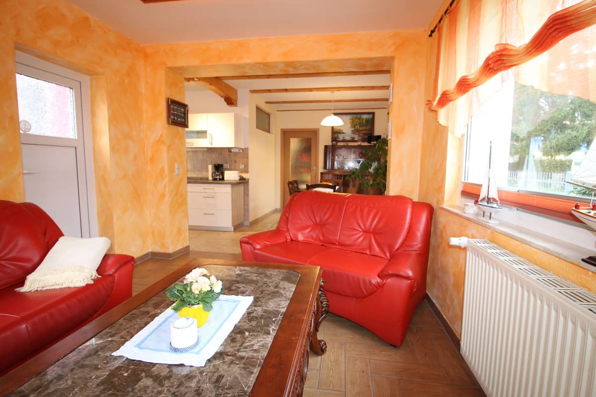 A living room with a red sofa, a coffee table with flowers, and a view of the kitchen and dining area.