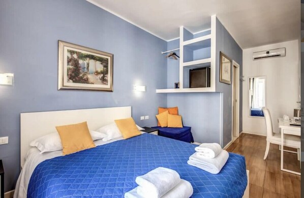 A hotel room with a large bed, a desk, and a chair. There is a painting on the wall and an air conditioning unit. - Residenza Giulia al Colosseo (Rome)