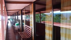 A covered corridor with benches and tables, large windows, and a view of greenery outside. - Hotel Green Mountain Turrialba (Turrialba)