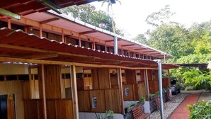 A covered outdoor seating area with wooden benches and stone walls, surrounded by greenery. - Hotel Green Mountain Turrialba (Turrialba)