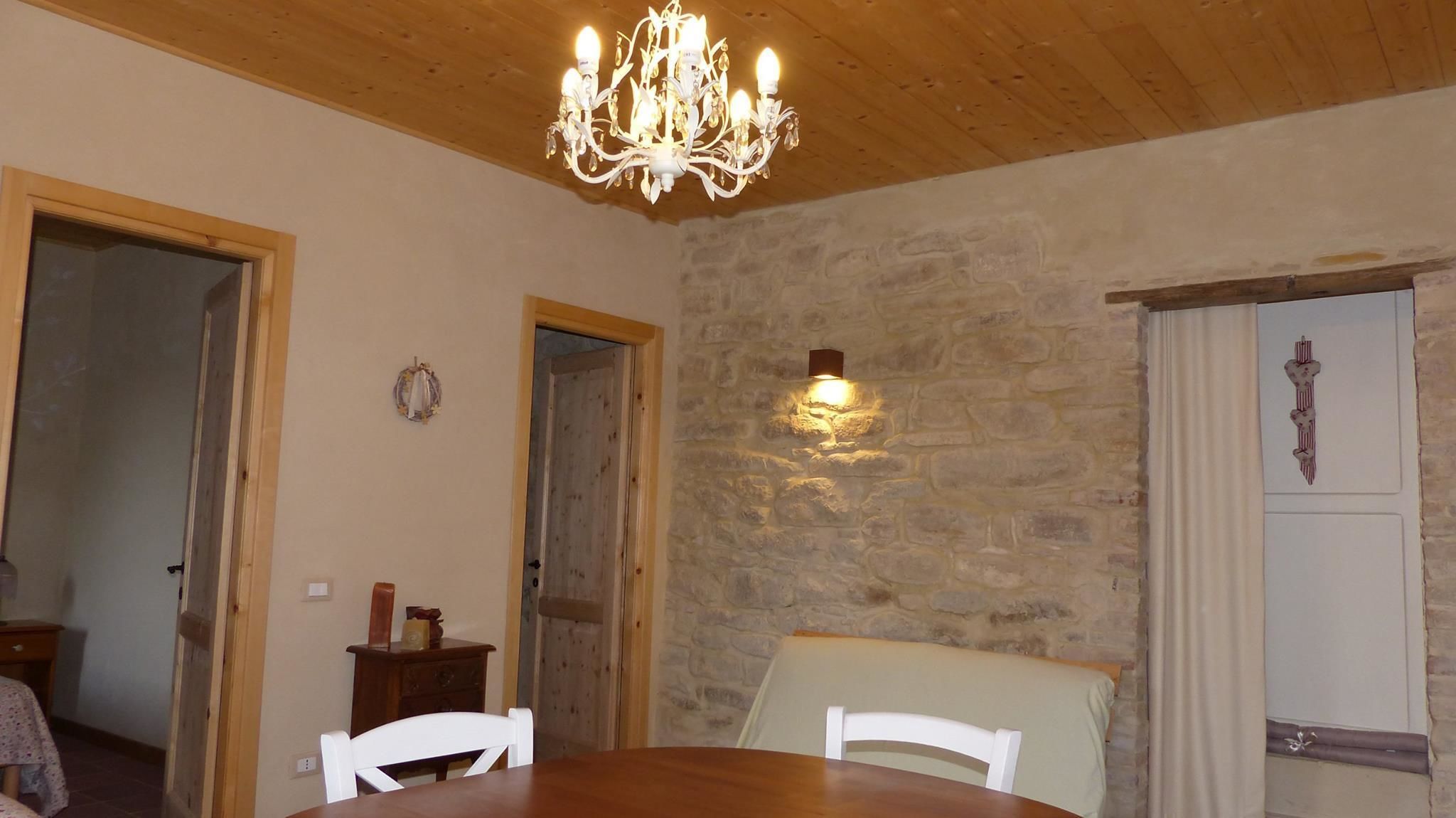 A dining room with a wooden ceiling, a chandelier, a stone wall, and a door with a cross.