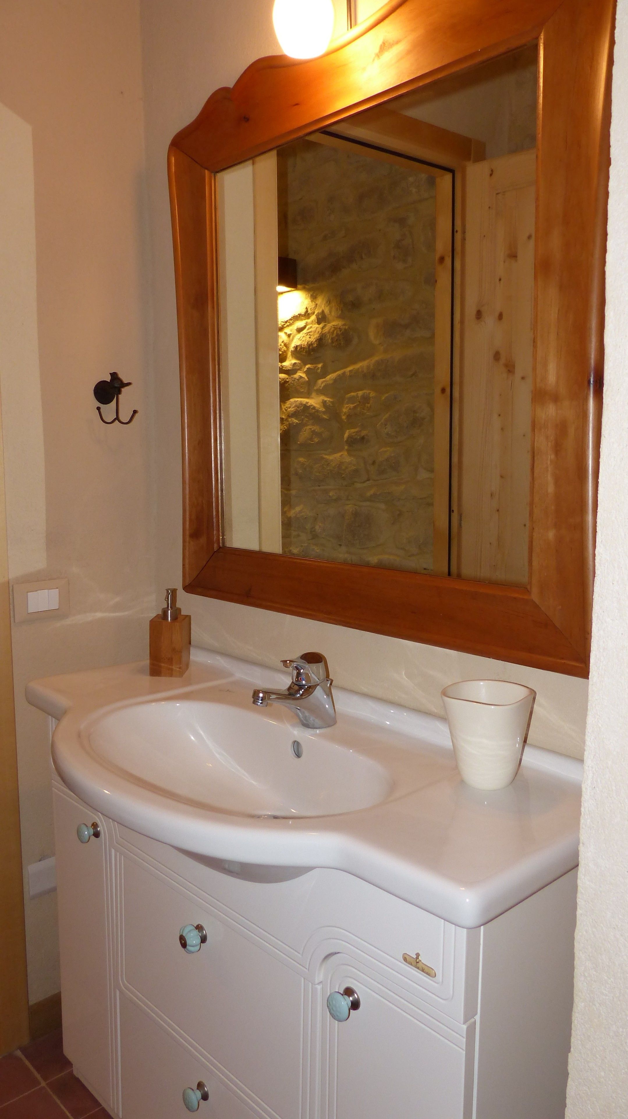 A bathroom with a white sink, wooden vanity, and a mirror with a stone wall reflection.