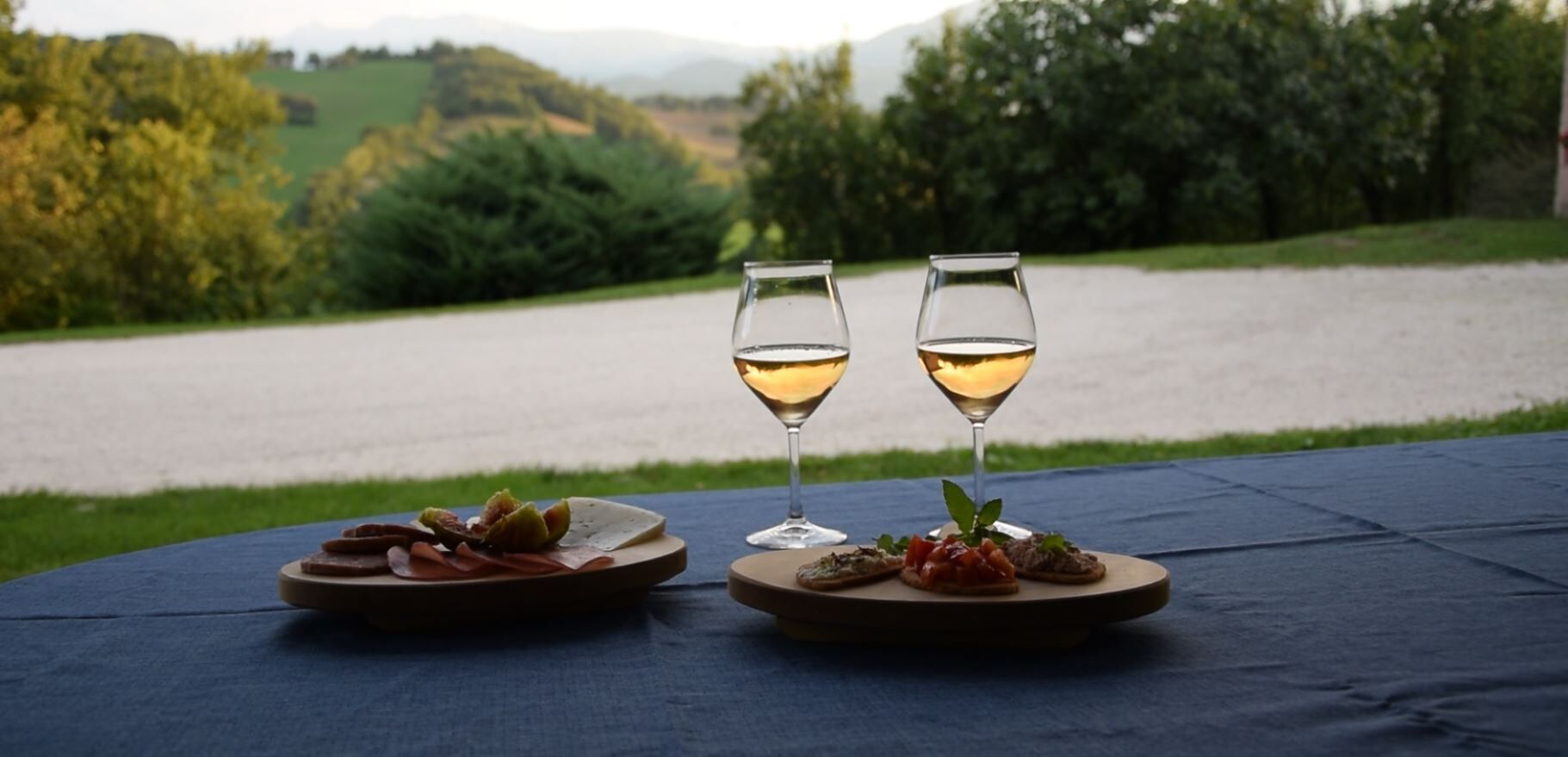 Two glasses of white wine on a table with plates of food.