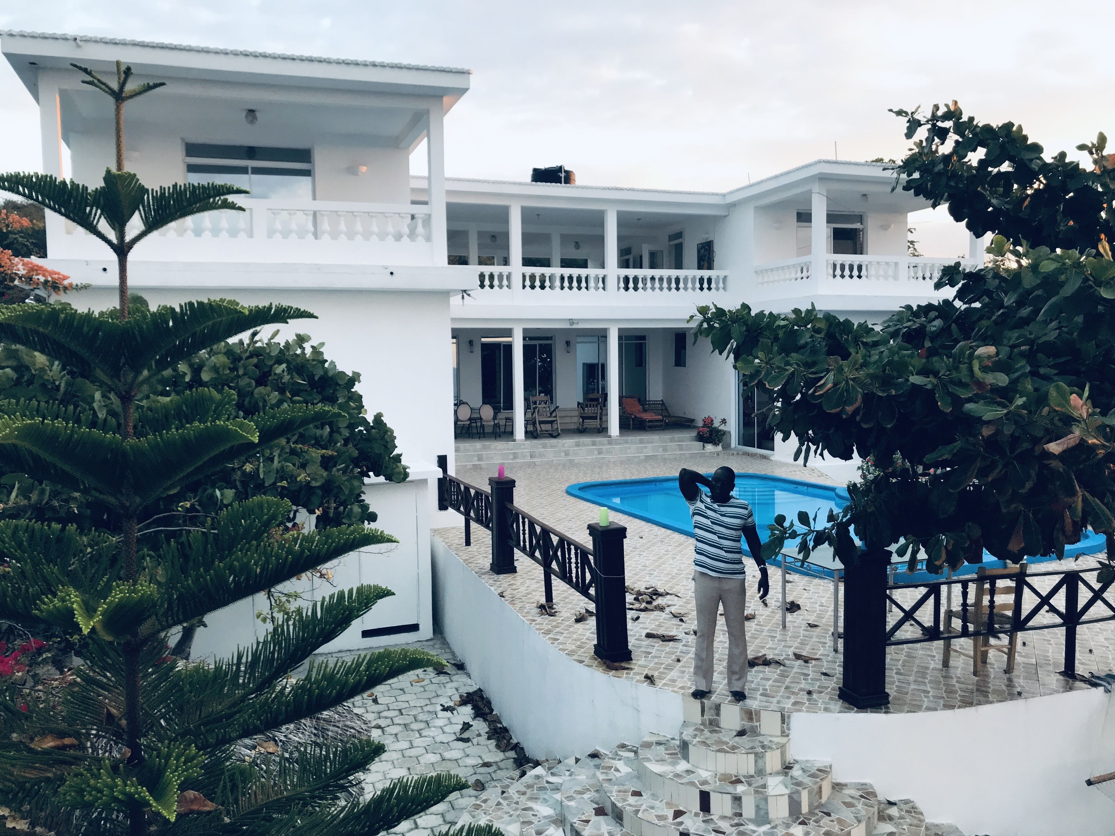 A modern white building with a swimming pool, surrounded by lush greenery and a stone pathway.