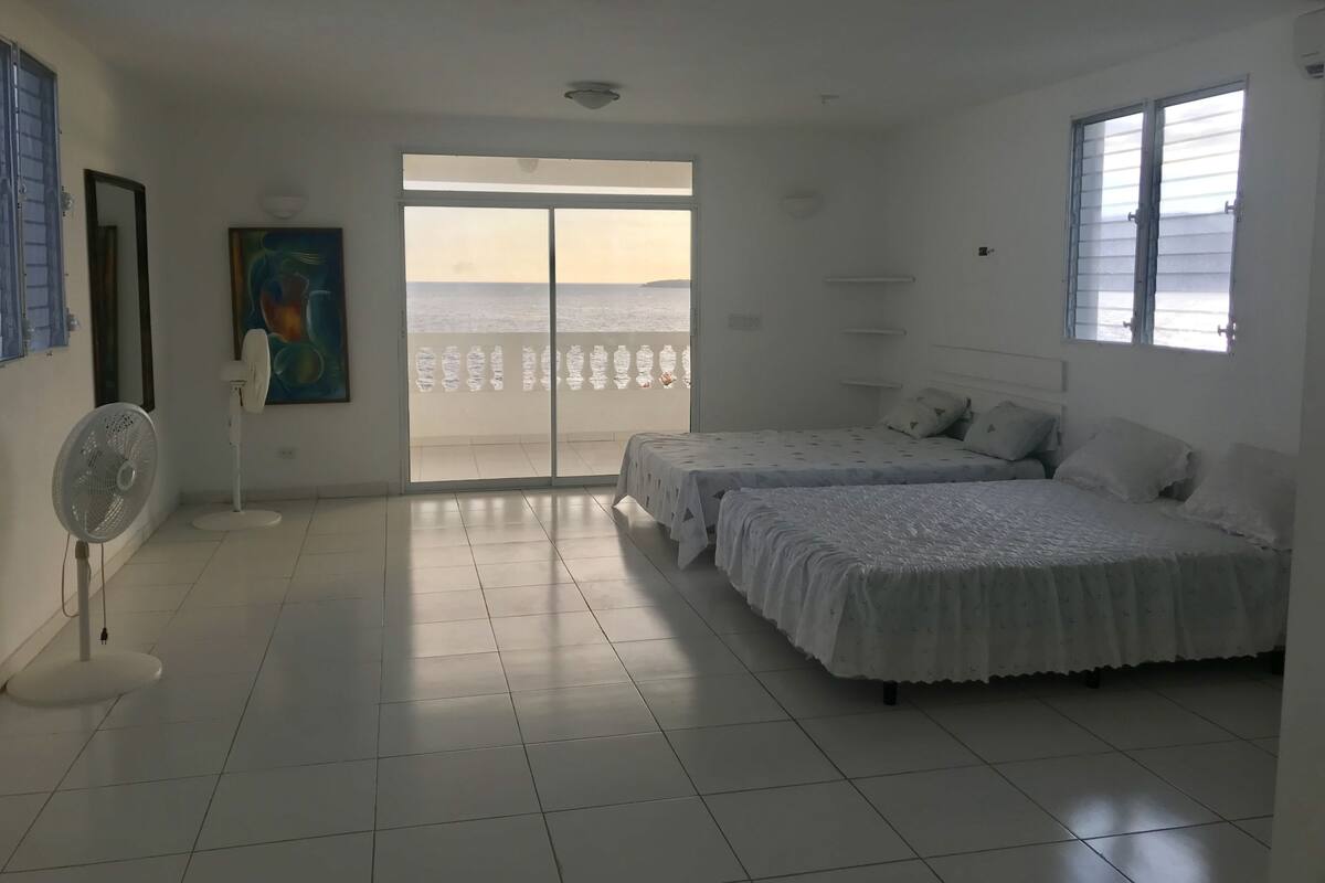 A hotel room with two beds, a large sliding glass door to a balcony, a ceiling fan, and a painting on the wall.
