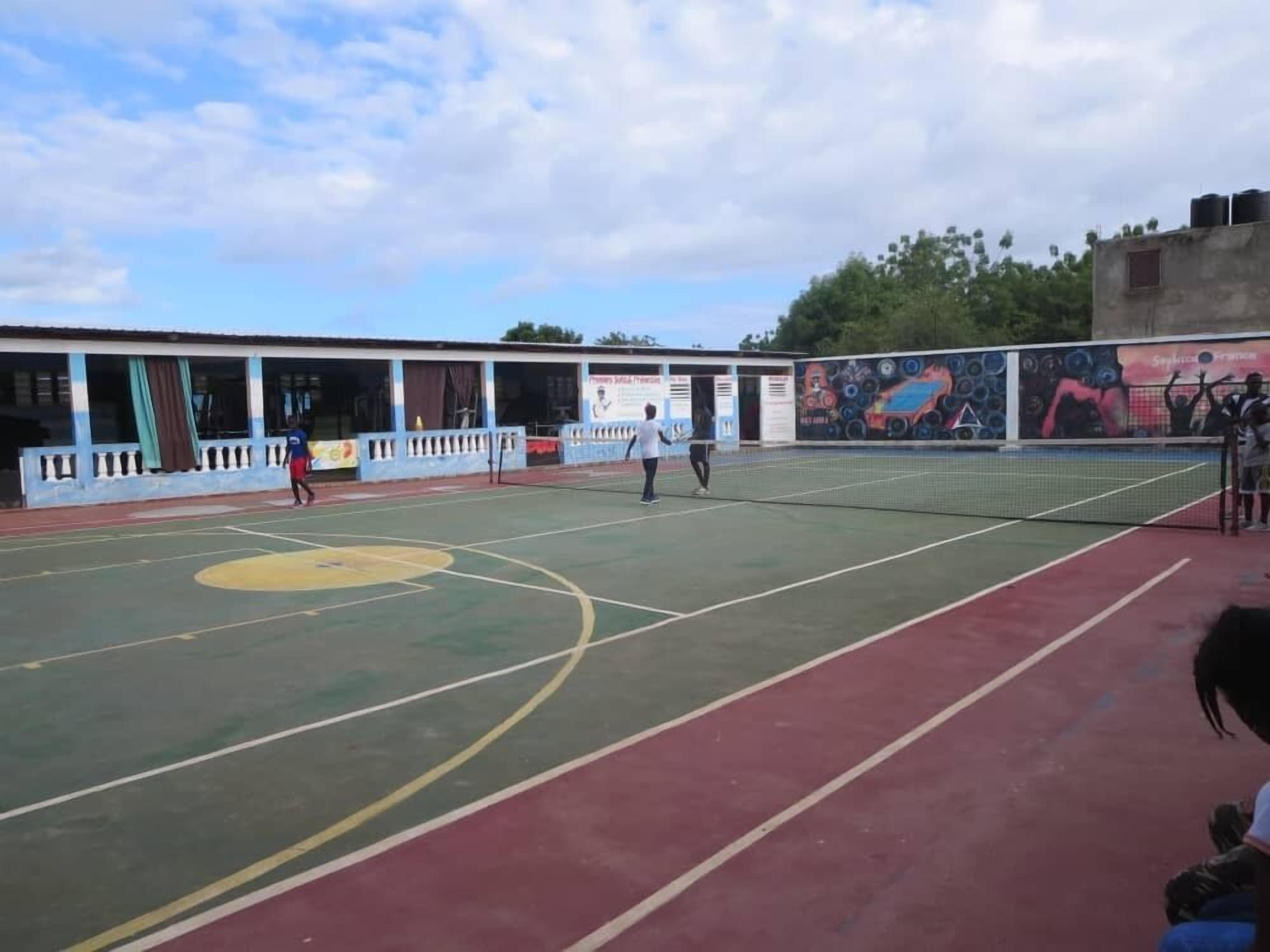 A sports court with a basketball court and a tennis court, surrounded by a building with a mural.
