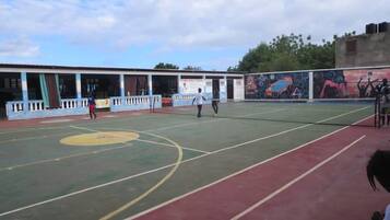 A sports court with a basketball court and a tennis court, surrounded by a building with a mural.