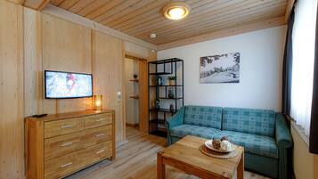 A wooden-paneled room with a wooden dresser, a green sofa, a wooden table with a plate of cookies, a black shelving unit, and a framed picture on the wall.