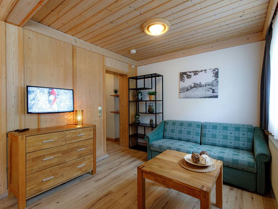 A wooden-paneled room with a wooden dresser, a green sofa, a wooden table with a plate of cookies, a black shelving unit, and a framed picture on the wall.