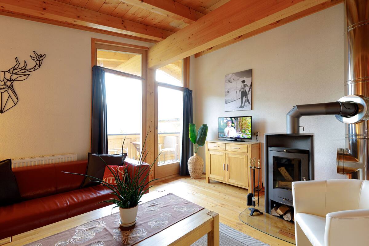 A cozy living room with a red sofa, a wooden coffee table, a fireplace, and a large window.
