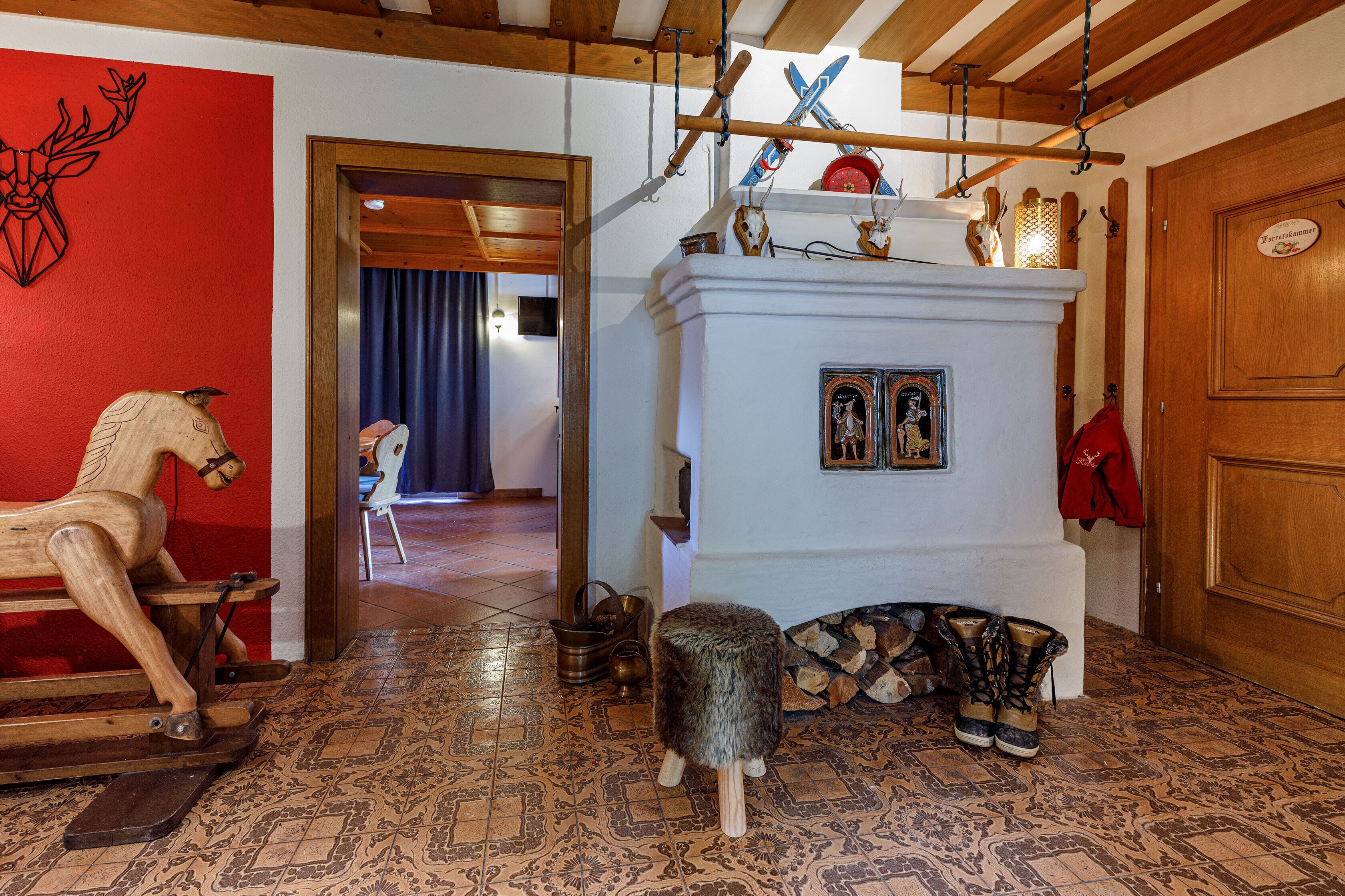 Un interno tradizionale con un cavalluccio a dondolo di legno, un caminetto bianco con legna da ardere e una parete rossa decorata con un'immagine di cervo.