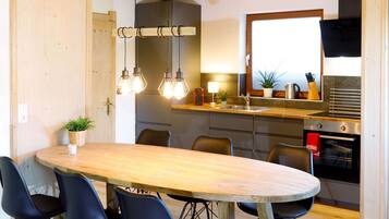 Una cocina moderna con una mesa y sillas de madera, un colgante de luz y un horno empotrado.