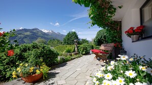 A patio with a stone floor, a wooden bench, and a potted plant with red flowers. - Landhaus Kitzblick (Piesendorf)