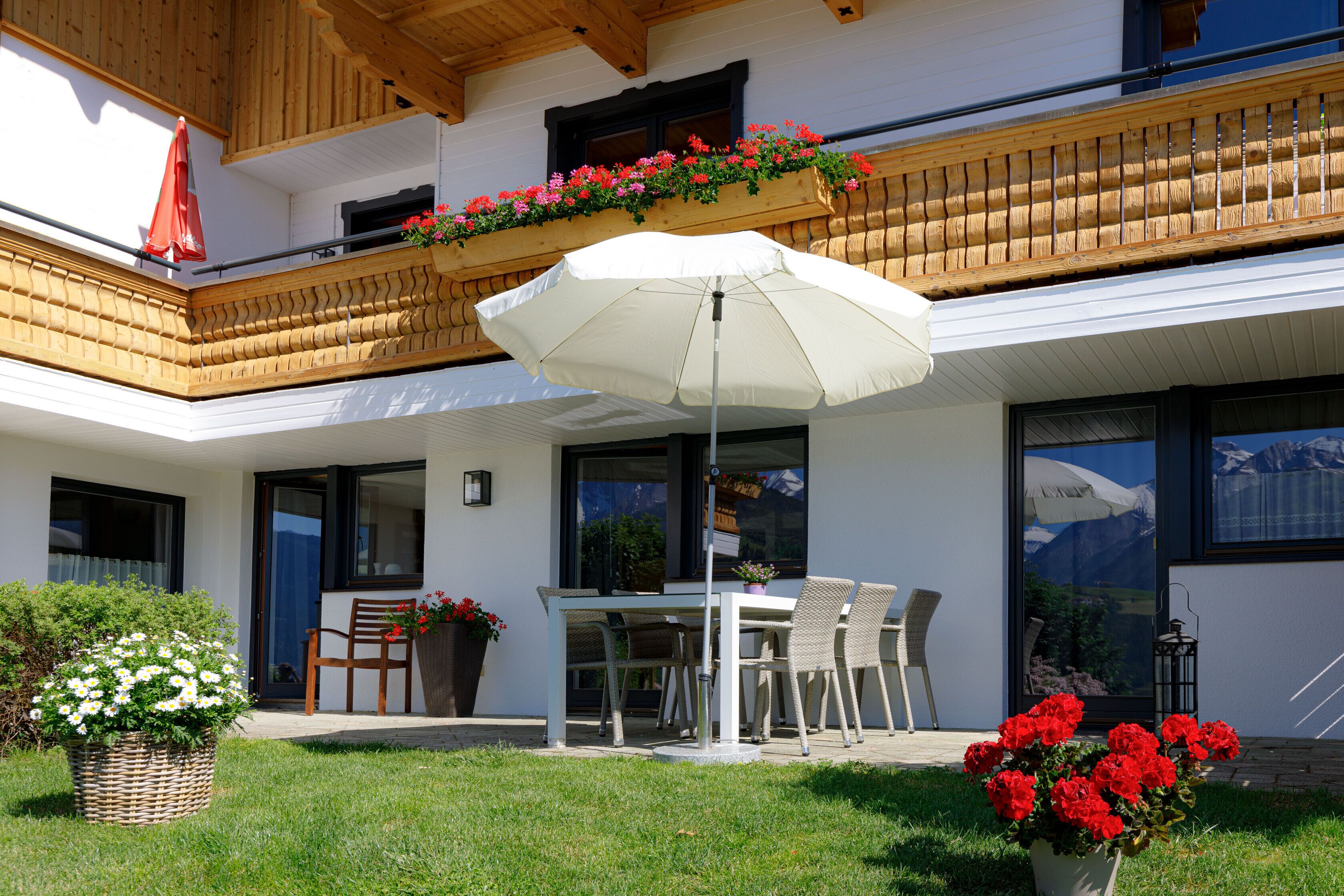A modern outdoor dining area with a table and chairs, a white umbrella, and potted plants.