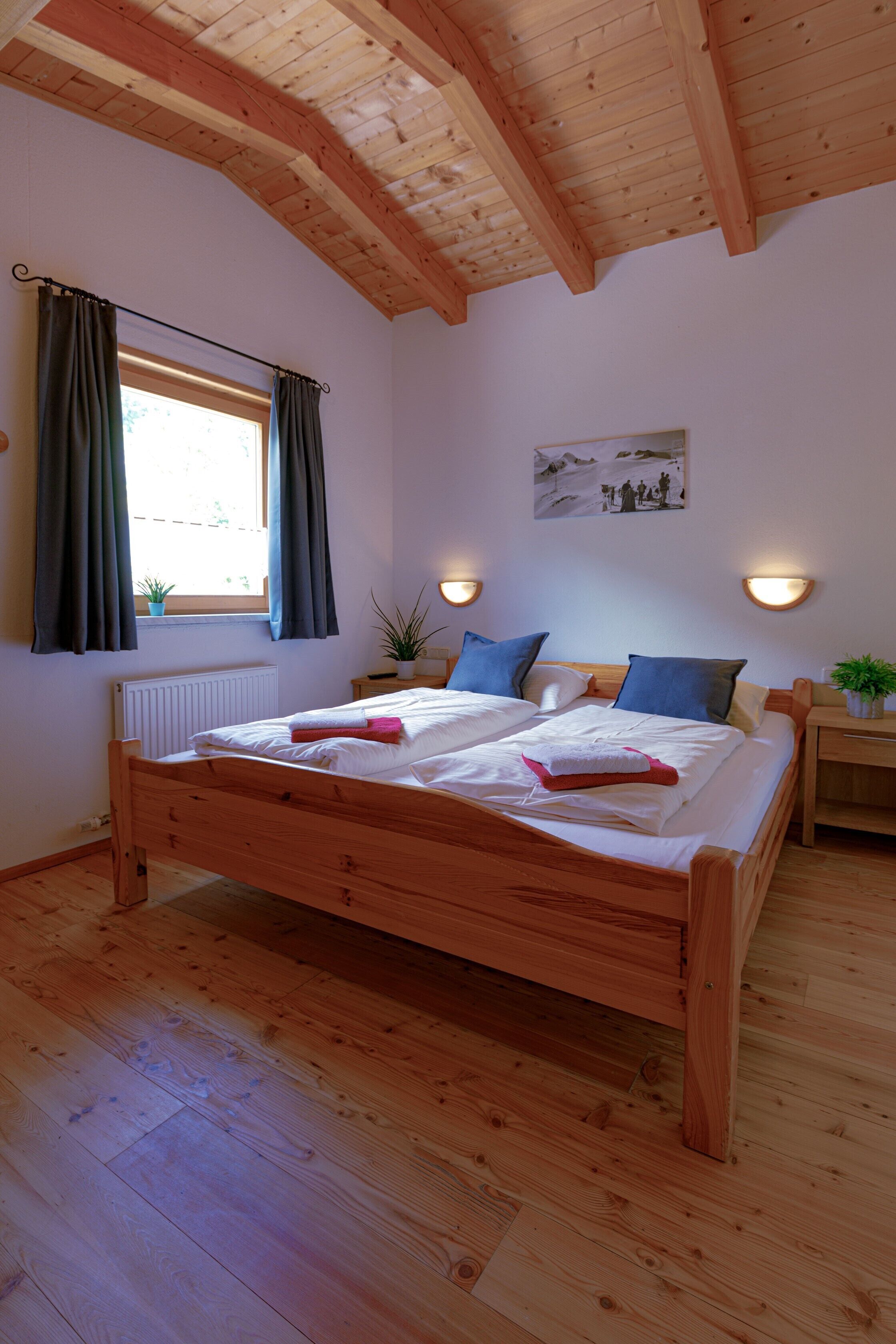 Un lit en bois avec deux oreillers, une table de chevet avec une lampe et une fenêtre avec des rideaux.