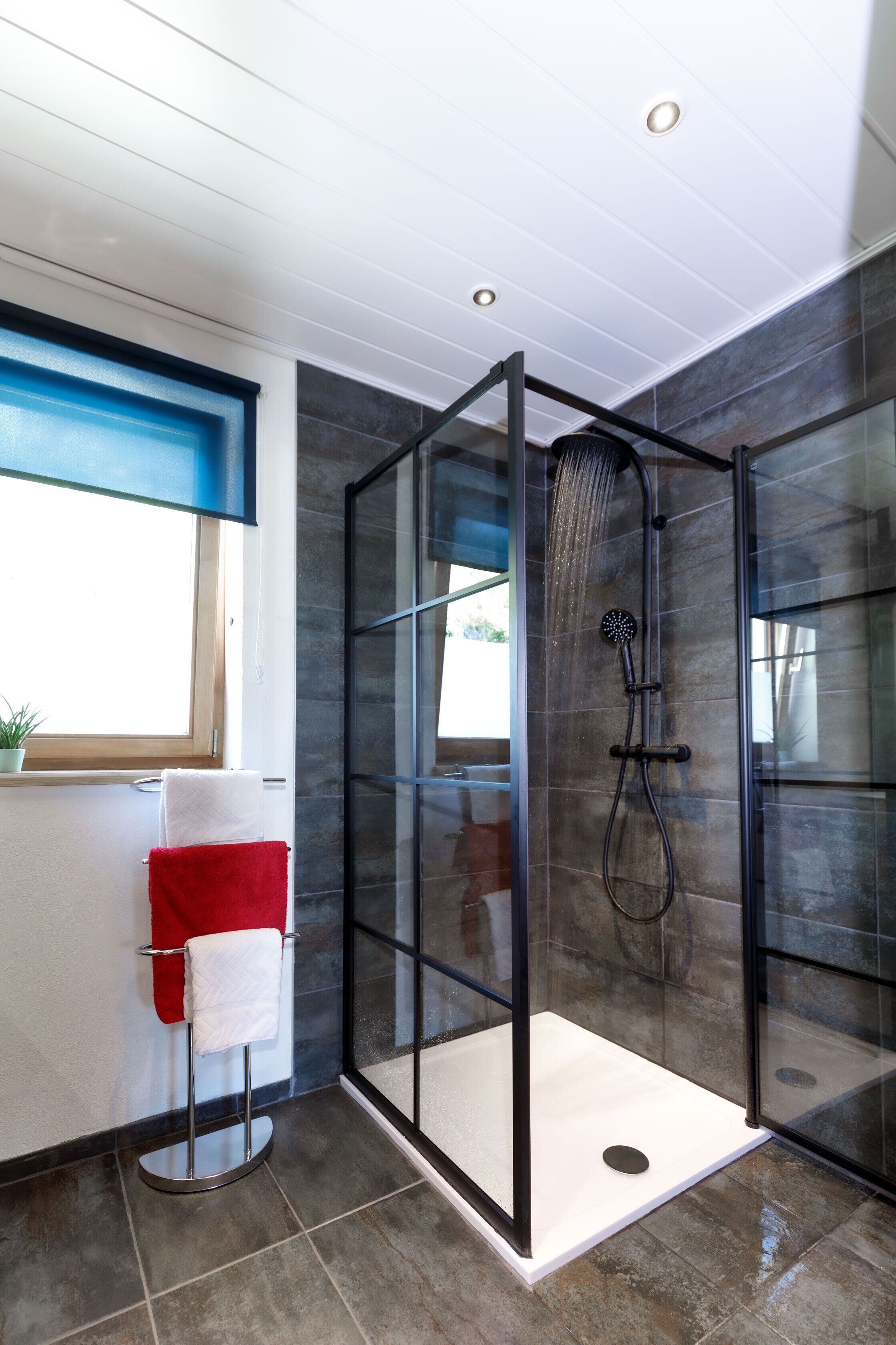 A modern bathroom with a glass-enclosed shower, a white sink, and a red towel on a towel rack.