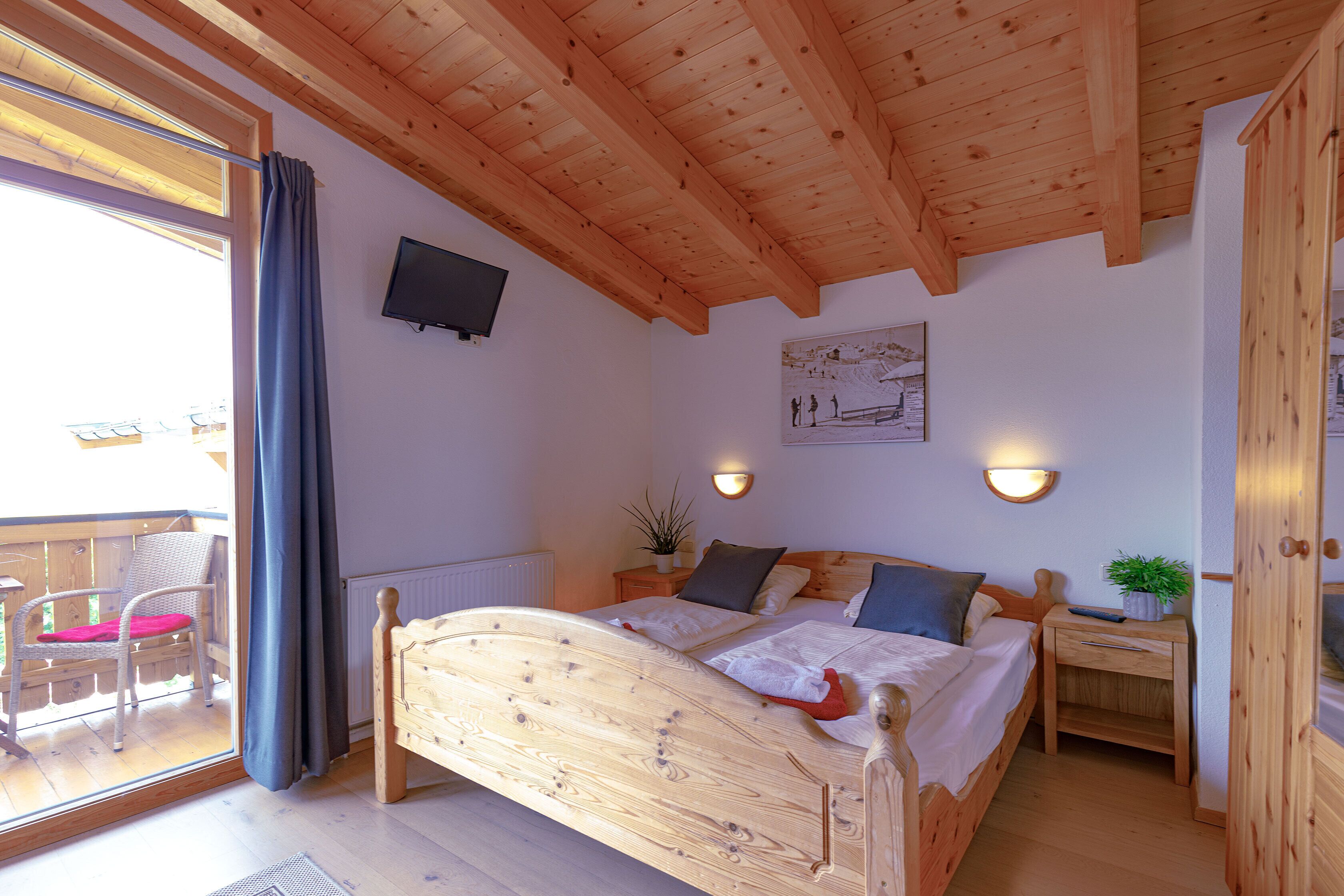 A wooden-framed bedroom with a bed, bedside table, and a small potted plant.