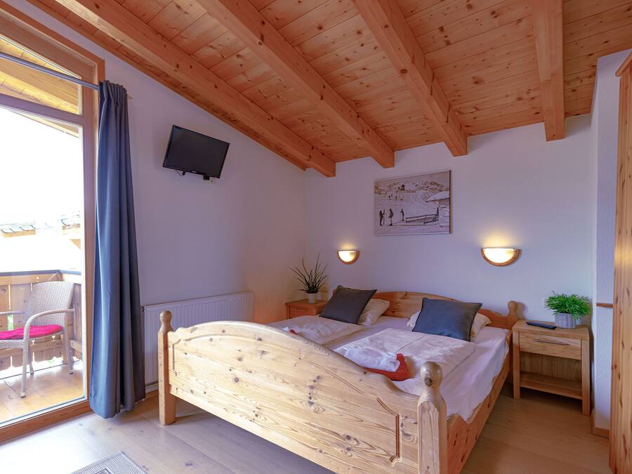 A wooden-framed bedroom with a bed, bedside table, and a small potted plant.