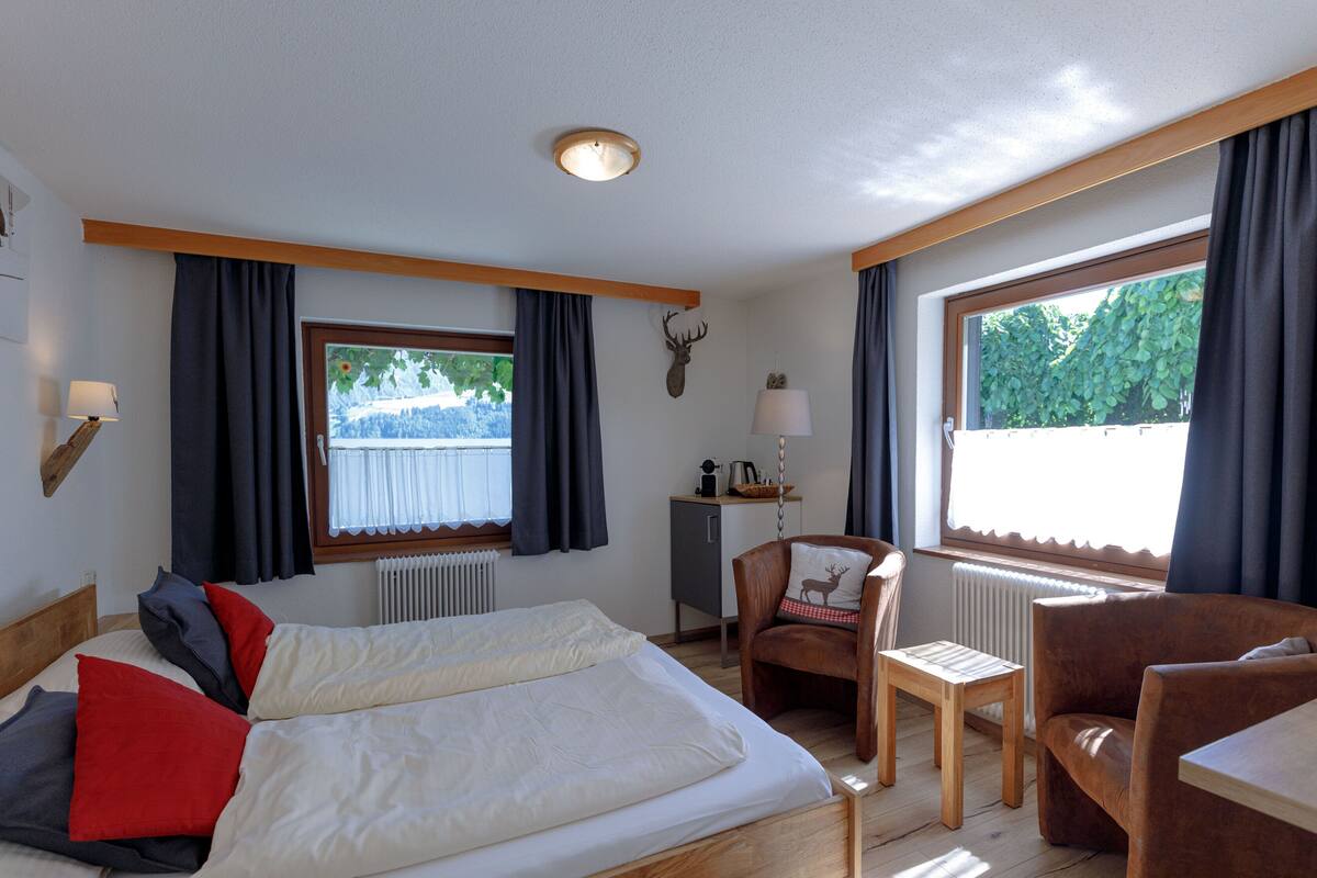 A hotel room with two beds, a desk, a chair, and large windows.