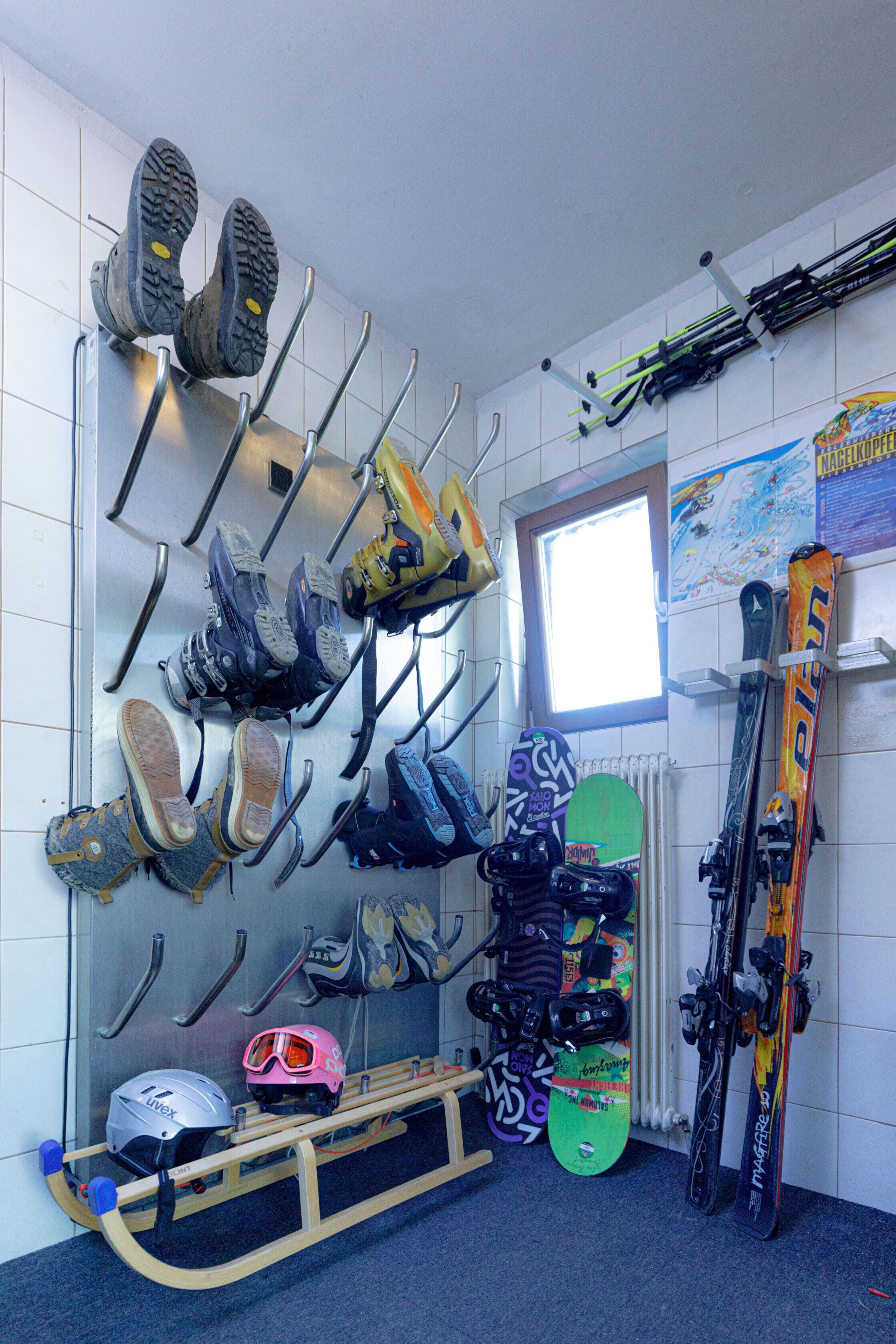 Een skiopslagruimte met meerdere skipaars en snowboards, een snowboardhouder en een ski rek met ski's en snowboards.