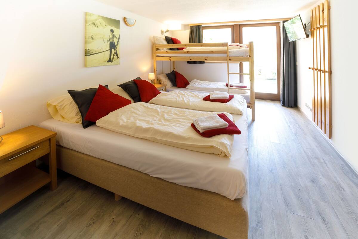 A dormitory room with bunk beds, a bedside table, a lamp, and a painting on the wall.