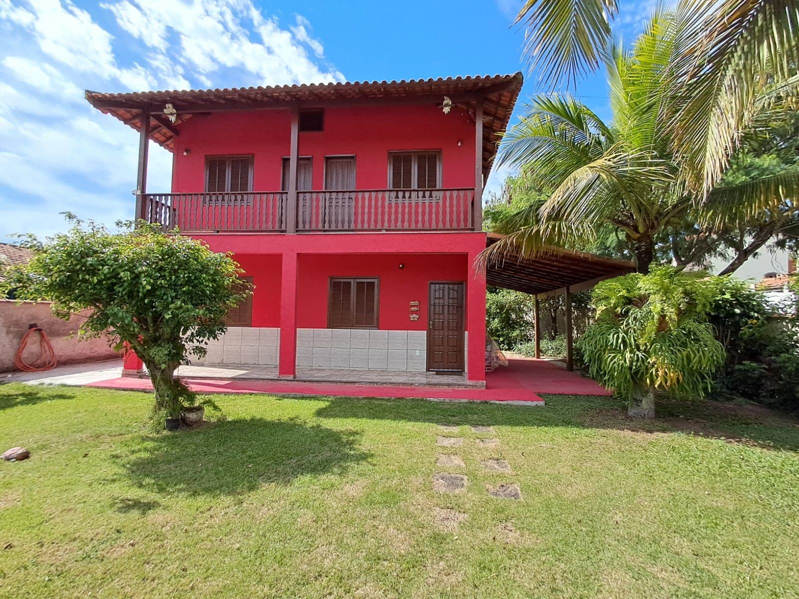 A two-story building with a red facade, a balcony on the upper floor, and a small tree in the front yard.