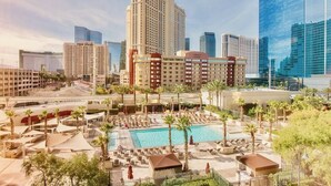 A hotel with a pool area, palm trees, and modern buildings in the background.