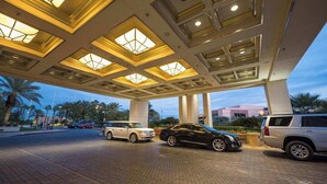 A hotel entrance with a covered parking area, palm trees, and a modern building in the background.