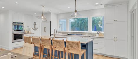 A modern kitchen with a central island, bar stools, and a dining area.