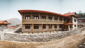 A multi-story stone building with a balcony, a stone wall in front, and a dirt path leading to it. - Kyirmu Lodge Phaplu (Phaplu)