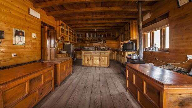 A wooden cabin-style kitchen with wooden cabinets, a central island, and a large window on the right. - Kyirmu Lodge Phaplu (Phaplu)