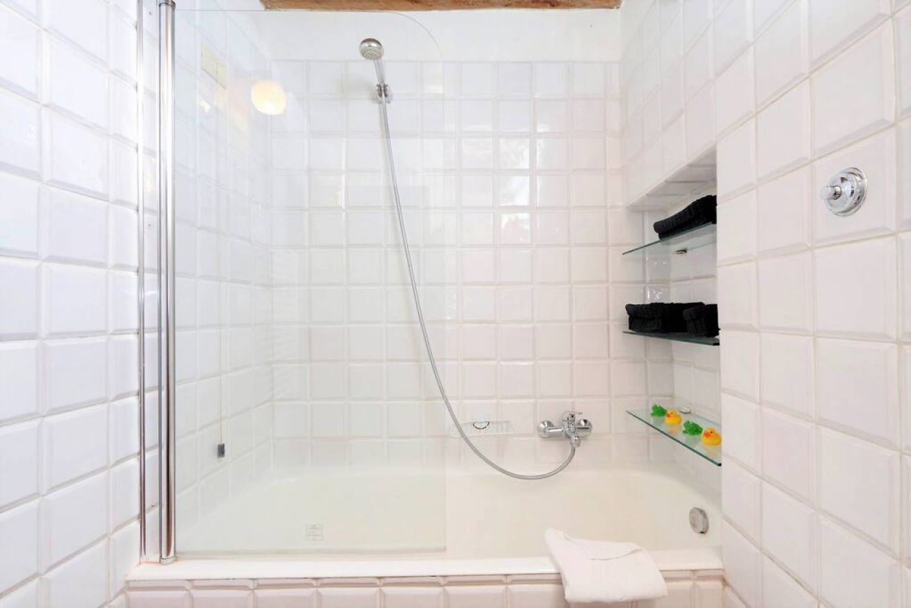 A glass-enclosed shower area with a bathtub, white tiled walls, and a glass shelf with toiletries.