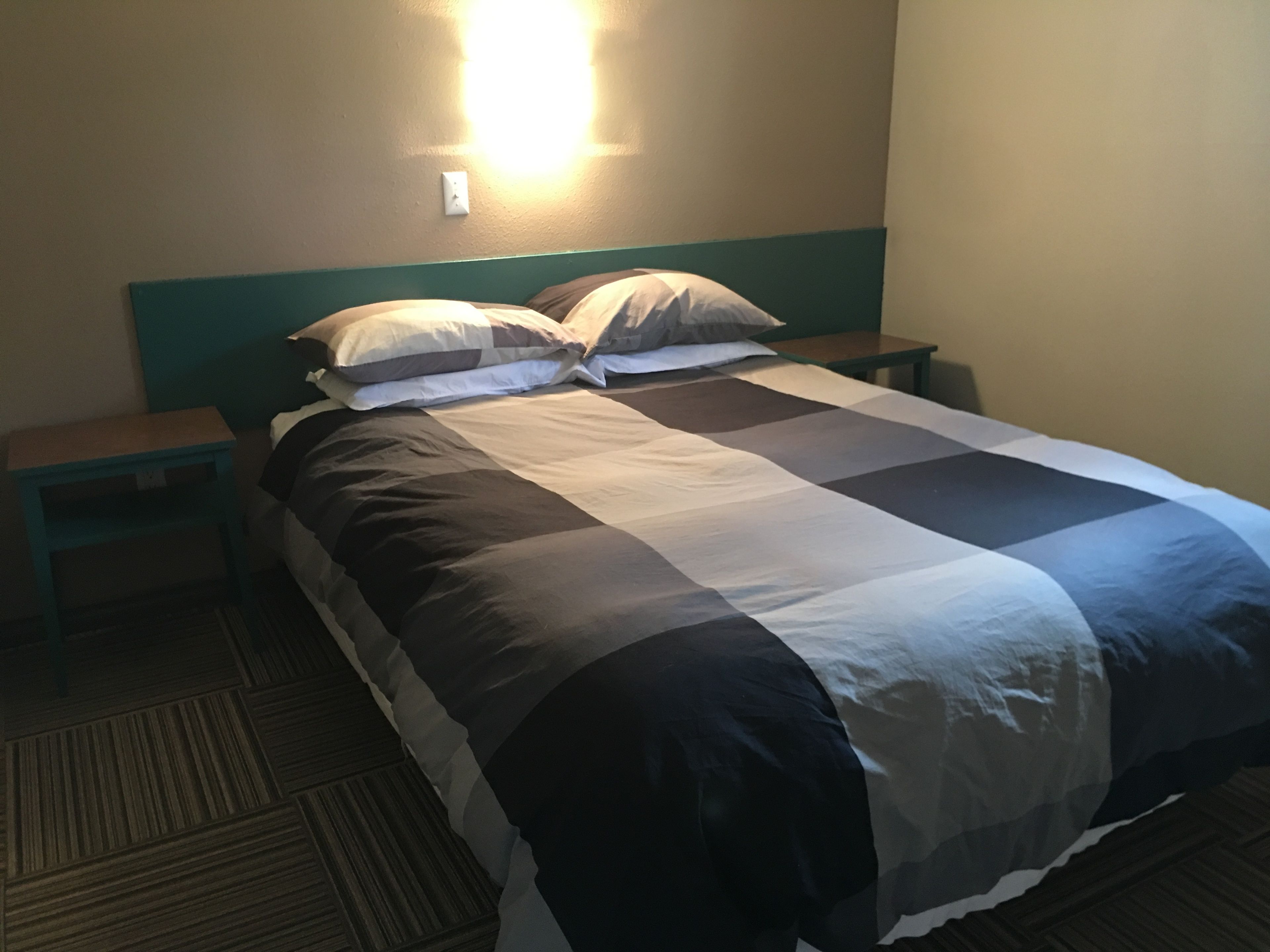 A neatly made bed with a checkered bedspread, two bedside tables, and a wall-mounted light fixture.