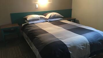 A neatly made bed with a checkered bedspread, two bedside tables, and a wall-mounted light fixture.