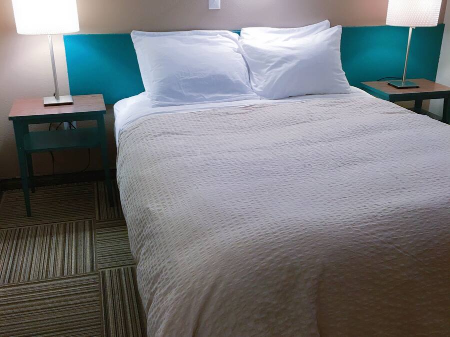 A neatly made bed with white linens, two bedside tables with lamps, and a patterned carpet.