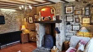 A cozy living room with a stone fireplace, wooden beams, and a fireplace mantel with various items.